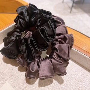 Close-up of pleated satin scrunchies in black and coffee brown on a wooden display tray