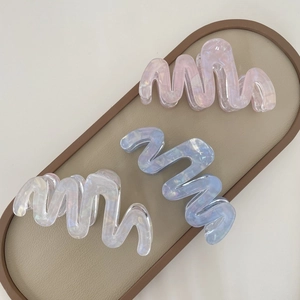 Three large wavy acetate hair claws in pink, blue and white on a leather tray