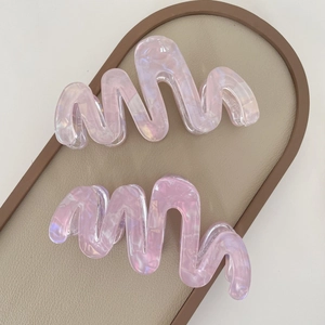 Detail of pink wavy acetate claw clips with pearl finish in a beige leather tray