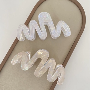 Close-up of wavy acetate hair claws with pearlescent finish in a display tray