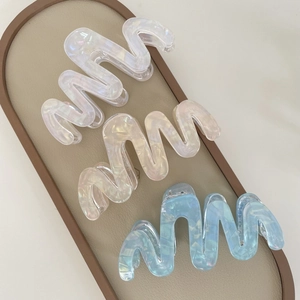 Close-up of three wavy acetate hair claws in iridescent white, pink, and blue on a tray