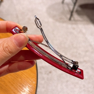 Macro shot of silver metal spring mechanism inside dark red glossy acetate hair clip
