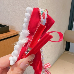 Detail einer roten Samt-Schleife mit Plüschrand, Erdbeerstickerei und Perlenanhängern