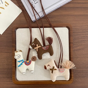 Handmade plush alpaca and pony charms with long neck straps on a wooden tray