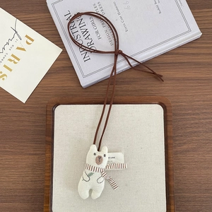 Close-up of a plush cream bear pendant with a brown striped scarf on a wooden table