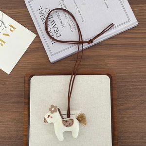 Detailed view of an embroidered fabric pony pendant necklace with tassel and brown cord