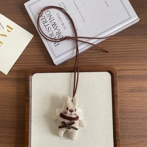 Detailed close-up of a handcrafted beige plush bunny pendant with a dark brown woven neck cord