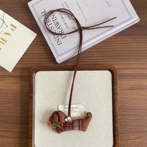 Close-up of a plush dachshund charm with red plaid clothes and a green bow on a tray