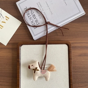 Detail of handmade cream plush pony charm with a checkered saddle and suede necklace cord