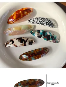 Dettaglio di fermagli per capelli ovali in acetato con texture retrò e scritta dorata