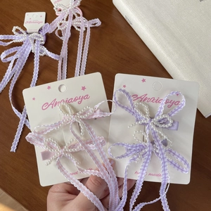 Close-up of pearl bow hair clip with pink checkered ribbon on display card