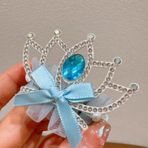 Detailed close-up of a child crown hair clip with blue gemstone and lace bow ribbon