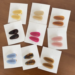Nine pairs of colorful matte teardrop hair clips on display cards over wood background