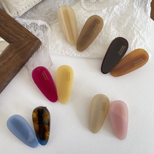 Close-up of matte teardrop hair clips in multiple colors with gold handmade lettering