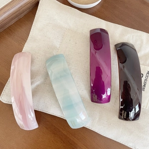 Set of four curved rectangle acetate hair clips in assorted marble colors on a beige pouch