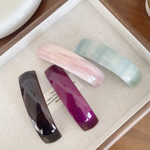 Detail of four acetate hair clips in black, purple, and marble patterns on a linen tray