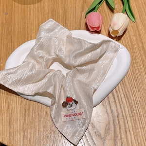 Detailed macro view of beige satin scrunchie with puppy embroidery on ceramic plate
