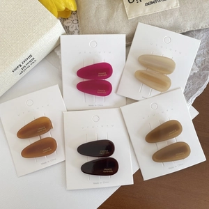 Detail view of water-drop hair clips in earthy matte tones on white display cards