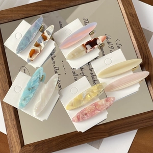 Close-up of eight diverse acetate hair clips with marble textures on a vintage tray
