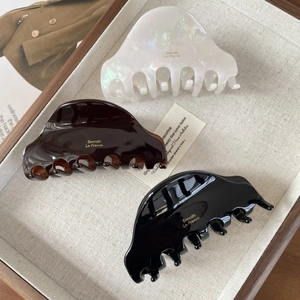 Three acetate shark hair clips in white pearl, tortoiseshell, and black with gold logo
