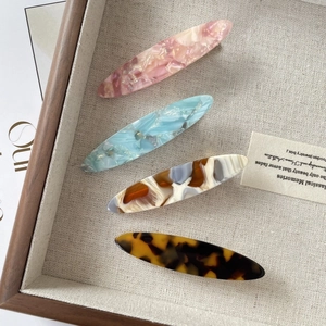 Close-up of four acetic acid hair clips in pink and tortoise patterns on a linen tray