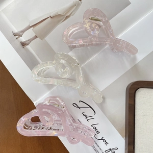 Iridescent heart-shaped hair claw clips in pearl pink and white on a wooden tray