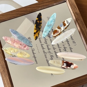 Assorted cellulose acetate hair clips with marble patterns displayed on a mirror