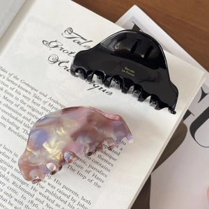 Detail of glossy black and marble acetate hair claws with gold lettering on a book