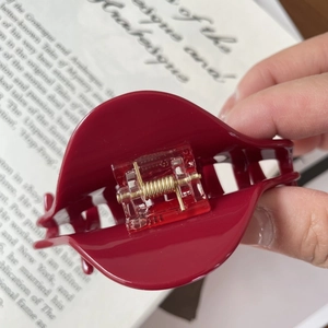 Detail view of the high-shine deep red claw clip with a premium golden metal spring mechanism