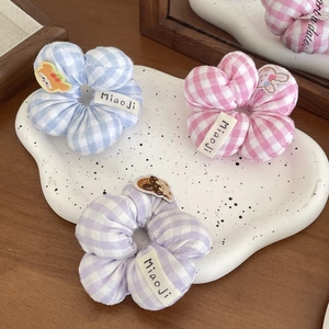 Dettaglio di tre elastici per capelli a fiori in quadretti vichy blu, rosa e viola