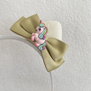 Dettaglio di cerchietto per bambini con fiocco in raso dorato e unicorno rosa colorato