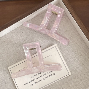 Detail view of large square marble pink hair claws on a wooden tray with linen fabric
