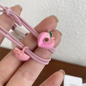 Dettaglio macro dell'elastico per capelli rosa con ciondolo a forma di pesca 3D e foglie