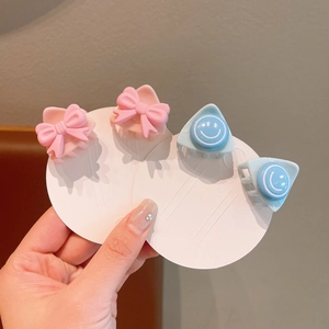 Detailed view of 4 mini hair clips featuring pink bows and blue smiley face designs