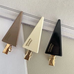 Close-up of three triangle acetate hair clips in brown, cream, and black colors