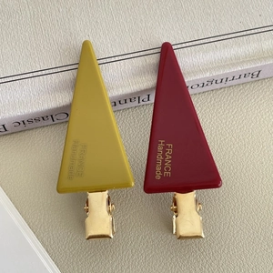 Detail view of mustard yellow and burgundy acetate hair clips with gold metal base