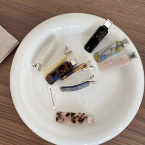 Detailed flat lay of French acetate hair clips with marble patterns in a white dish