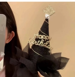 Detalle de un gorro de cumpleaños negro con purpurina, texto dorado y borde de encaje