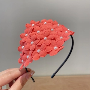 Detailed close-up of coral pink fabric flowers with pearls on a slim black headband