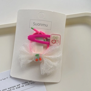 Detail of pink hair clip and bow hair tie with cherry pattern on brand card