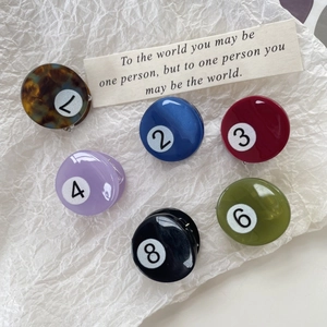 Colorful mini billiard ball hair clips featuring numbers on a white textured background