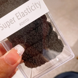Détail d'un chouchou noir à texture popcorn présenté dans sa boîte cadeau transparente