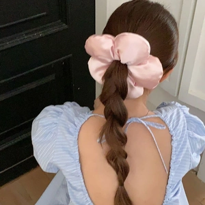 Rear view of large pink satin flower scrunchie holding a low ponytail in style
