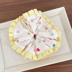 Détail d'un chouchou en tissu avec motifs cœurs colorés et bordure en dentelle jaune