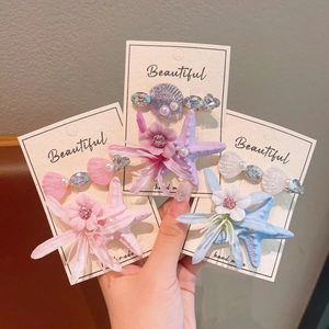 Macro detail of starfish, shell, and floral hair clips set with pearls in macaron colors