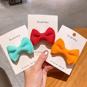 Close-up of three colorful bow hair clips in red, mint, and orange on display card