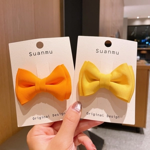 Handmade candy-colored bow hair clips in orange and yellow on a white display card