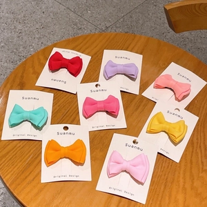 Set of 8 colorful candy-colored bow hair clips on display cards over a wooden surface