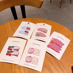 Close-up of five pairs of sweet fabric hair clips with cherry and bear designs on wood