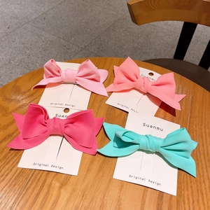 Detailed set of four matte finish bow hair clips in pastel colors on a wood surface